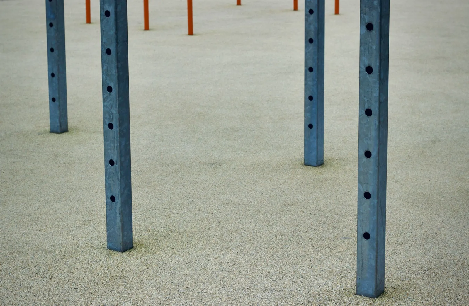 Close view of steel poles with round holes on a textured concrete surface, minimalist design.